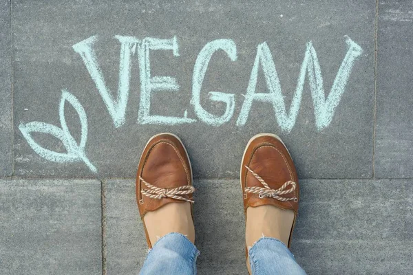 Pies femeninos con texto vegano escrito en la acera gris — Foto de Stock
