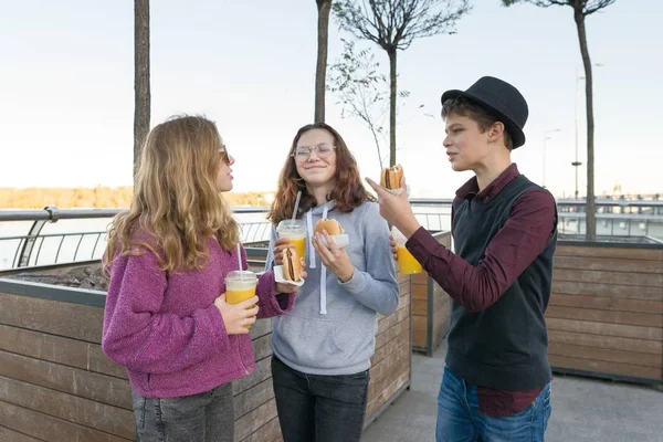 Chłopiec i dwie dziewczyny na ulicy miasta z hamburgery i sok pomarańczowy — Zdjęcie stockowe