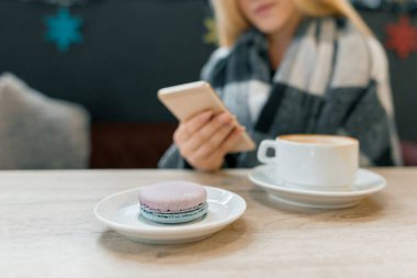 Tabakta Macaroon, kahve fincanı, akıllı telefon ile yünlü battaniye güzel sarışın kız