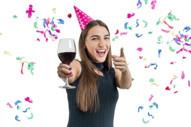 Genç güzel beyaz zemin üzerine kırmızı şarap ile esmer kadın gülümseyerek ve parti şapka puan, parmağını giyen izole. Parti, içecekler, tatil ve kutlama kavramı
