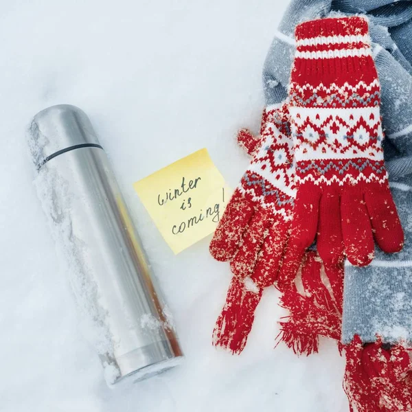 L'hiver arrive, texte sur l'autocollant. Fond d'hiver - dans la neige une écharpe, gants, thermos . — Photo