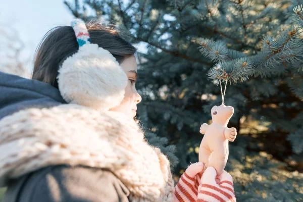 Invierno retrato al aire libre de niña cerca del árbol de Navidad, chica sonriente decora árbol de Navidad con juguete, hora dorada —  Fotos de Stock