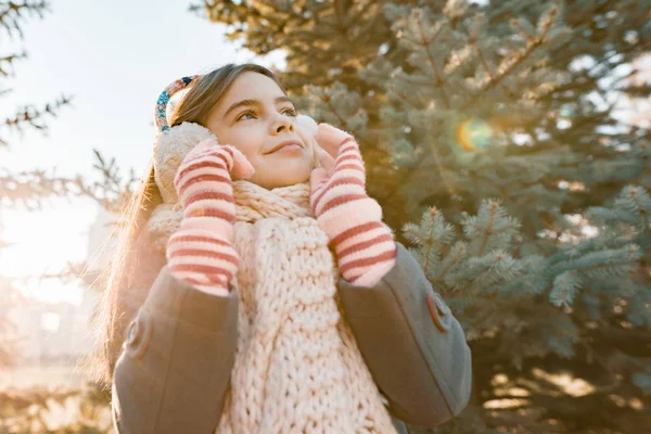 Retrato de invierno al aire libre de una niña sonriente en una bufanda de punto cerca del árbol de Navidad, hora dorada —  Fotos de Stock