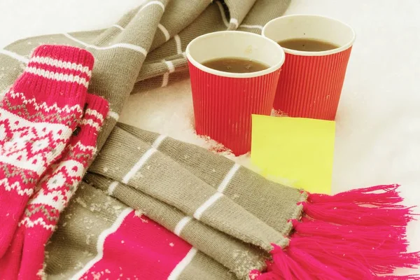 Heure d'hiver, écharpe de vêtements chauds et mitaines dans la neige, avec deux tasses de café. Autocollant jaune propre pour texte — Photo