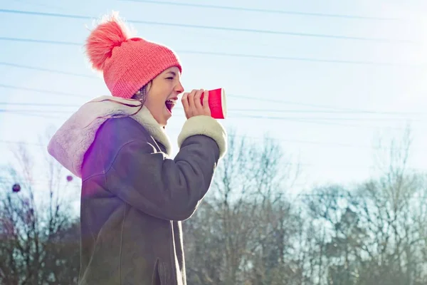 Invierno al aire libre retrato de niña gritando en una taza de papel megáfono, espacio de copia —  Fotos de Stock