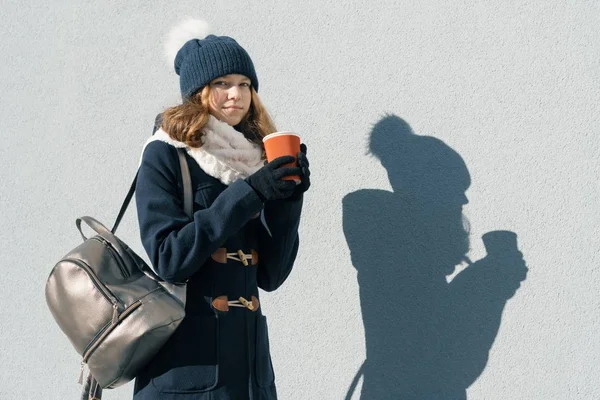 Invierno soleado retrato al aire libre de adolescente con un abrigo y sombrero de punto con taza de bebida caliente, espacio para copiar —  Fotos de Stock