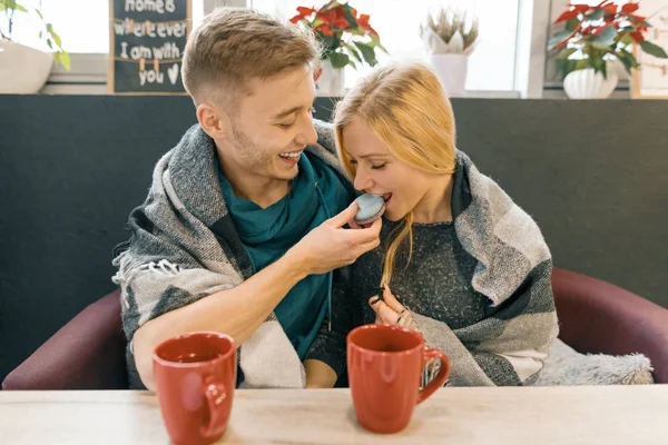 Jovem casal feliz apaixonado no café, jovem e mulher juntos sorriem abraçando, bebendo chá de café comendo macaroons — Fotografia de Stock