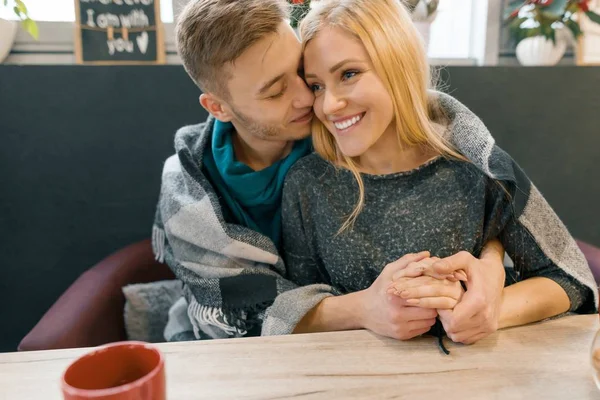 Retrato de inverno outono de jovem casal abraçando. Jovem e mulher no café sob cobertor de lã quente bebendo chá de café, felizes juntos — Fotografia de Stock