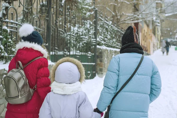 겨울 가족이 도시에서 걷고, 어머니와 딸은 눈 덮인 도시 거리를 따라 걷습니다. — 스톡 사진