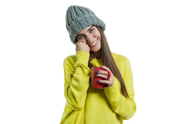 Portrait of smiling winter young woman in knitted hat, yellow sweater with cup of hot drink, isolated on white — Stock Photo, Image