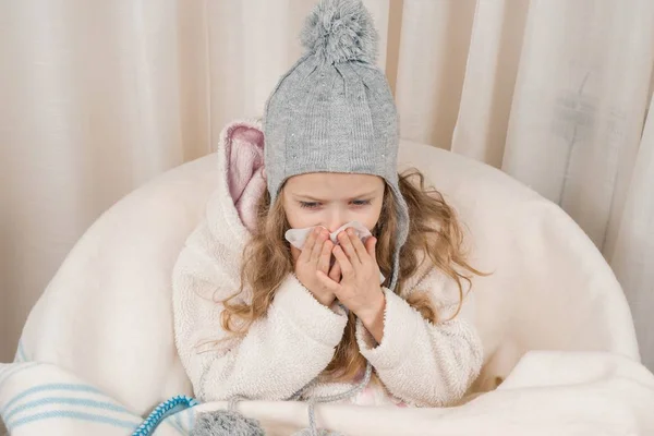 Enfant fille à la maison dans la chaise avec chapeau chaud en laine couverture éternuements en mouchoir. Saison automne hiver rhumes — Photo