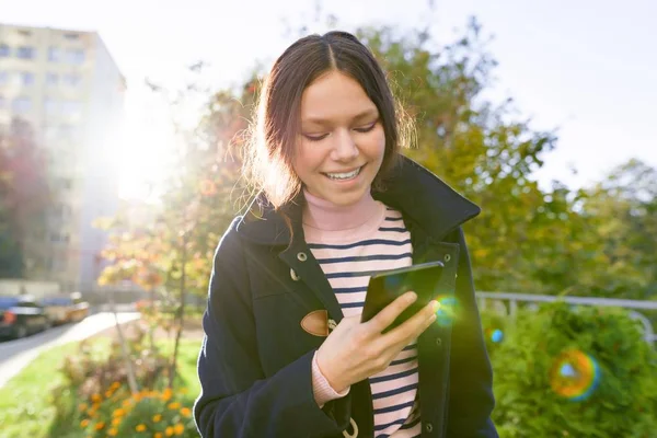 Teen κορίτσι στο παλτό χρησιμοποιώντας smartphone, Ηλιόλουστη μέρα του φθινοπώρου — Φωτογραφία Αρχείου