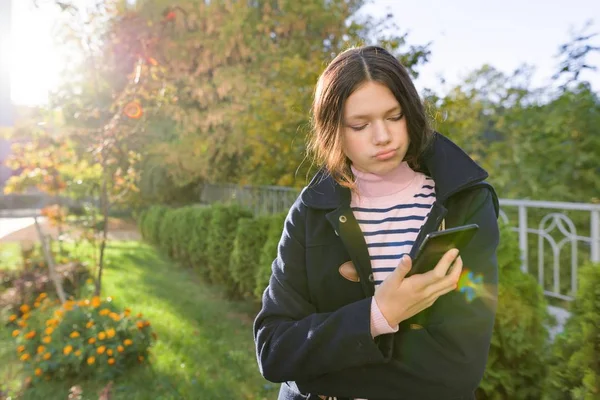 Chica adolescente con abrigo usando teléfono inteligente, día soleado de otoño —  Fotos de Stock