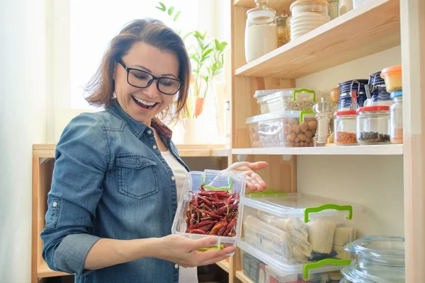 Kvinna i skafferi hållande behållare med röd bitter chilipeppar — Stockfoto