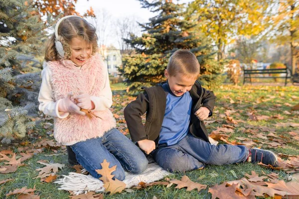 Niños felices jugando y sentados sobre hojas amarillas — Foto de Stock