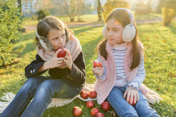 Children two girls eating red apples in yellow autumn park