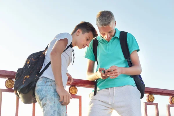 Dos amigos adolescentes usando smartphone, hablando y sonriendo —  Fotos de Stock