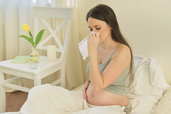 Young pregnant woman with handkerchief sitting in bed at home