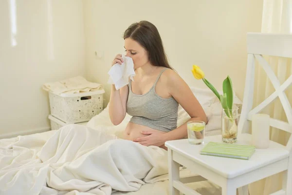 Mujer embarazada joven con pañuelo sentado en la cama en casa — Foto de Stock