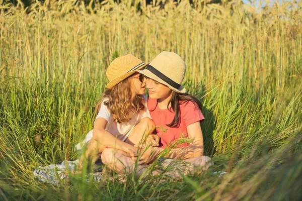 Две улыбающиеся девушки сидят в траве, дети разговаривают — стоковое фото