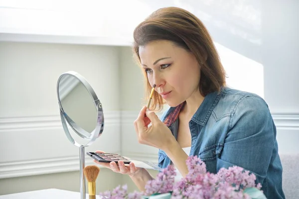 Rijpe vrouw kijkt naar haar gezicht in spiegel, make Makeup — Stockfoto