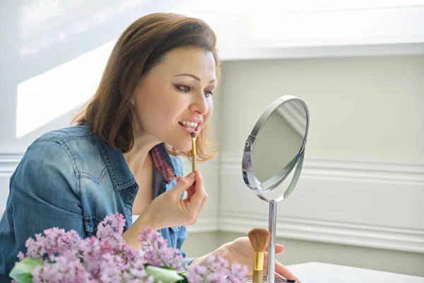 Mujer madura mirando su cara en el espejo, haciendo maquillaje —  Fotos de Stock