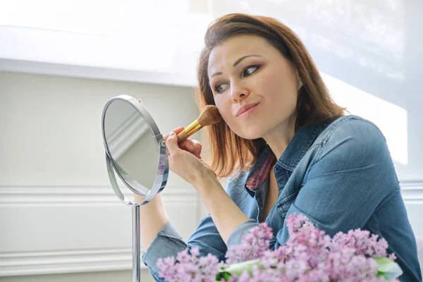 Rijpe vrouw kijkt naar haar gezicht in spiegel, make Makeup — Stockfoto