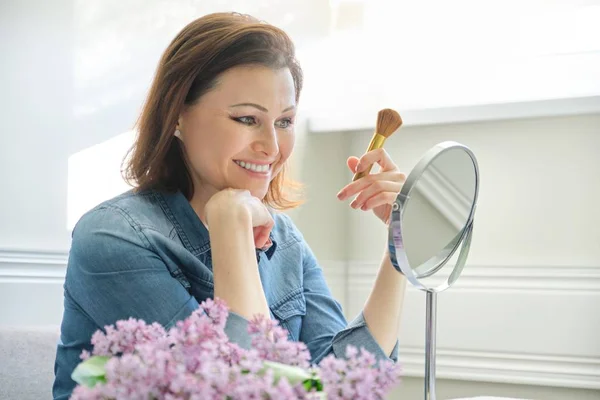 Rijpe vrouw kijkt naar haar gezicht in spiegel, make Makeup — Stockfoto