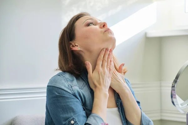 Retrato de mujer madura con espejo de maquillaje masajeando su cara y cuello —  Fotos de Stock