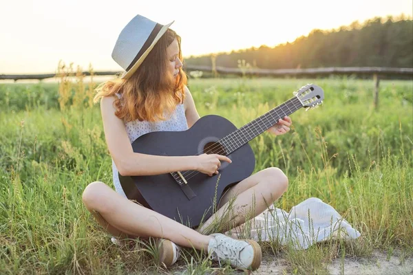 Teenager girl in hat playing the guitar nature background — Stock Photo, Image