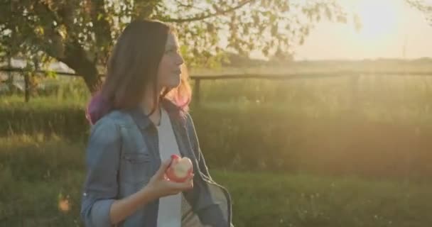 Joven chica feliz caminando y comiendo manzana roja — Vídeo de stock