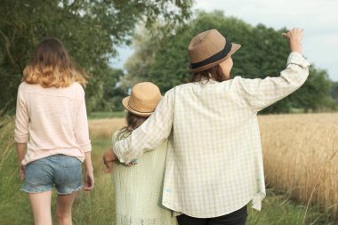 Anne ve iki kızı birlikte kırsal yol boyunca yürüyüş, geri görünümü