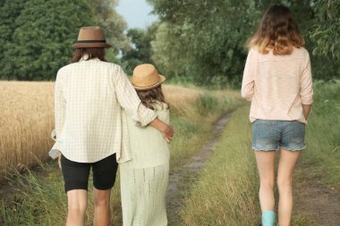 Anne ve iki kızı birlikte kırsal yol boyunca yürüyüş, geri görünümü