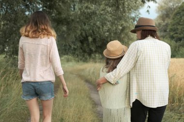 Anne ve iki kızı birlikte kırsal yol boyunca yürüyüş, geri görünümü