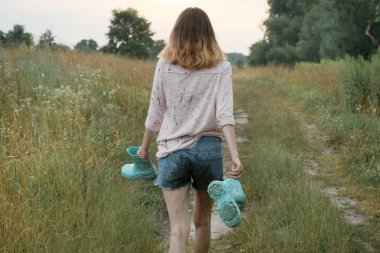 Elinde botlarla kırsal yolda yürüyen genç kız