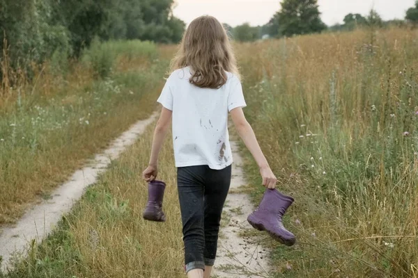Niña caminando por el camino rural con botas de lluvia en las manos —  Fotos de Stock