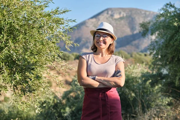 Portrait of confident woman olive farm owner, background olive trees in the mountains