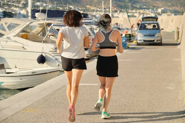 View of the back of mother and daughter running at seaside promenade — Stock Photo, Image