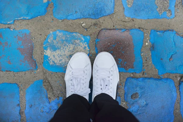 Legs of woman in white sneakers on vintage blue painted pavers — Stock Photo, Image