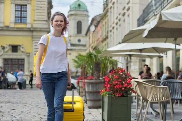 Girl walking with backpack and yellow suitcase on city street — Stock Photo, Image