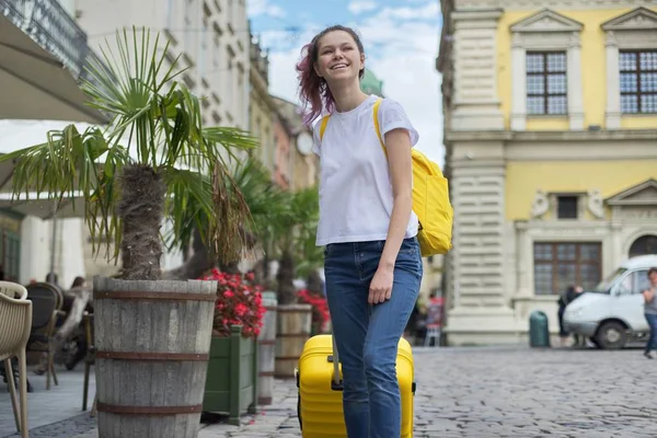 Chica caminando con mochila y maleta amarilla en la calle de la ciudad — Foto de Stock