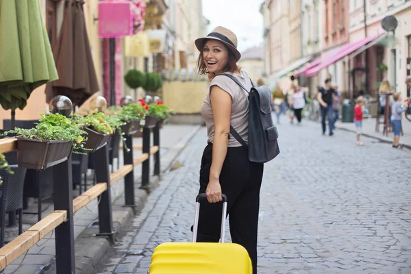 Mature smiling woman traveling in tourist city with suitcase — Stock Photo, Image