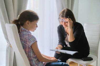 Talking girl and woman psychotherapist in office near window