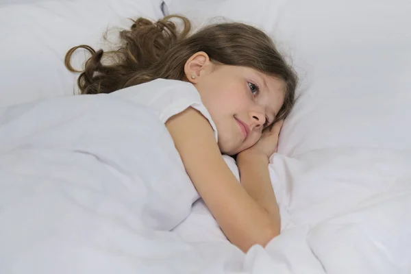 Улыбающаяся красивая девочка лежит на подушке, белая кровать, крупным планом лицо — стоковое фото