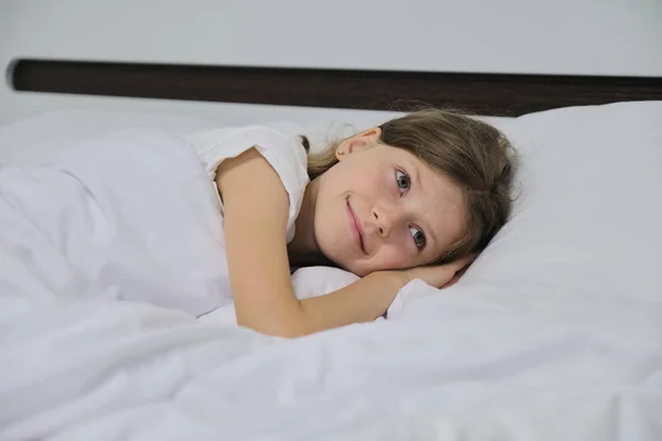 Smiling beautiful child girl lying on a pillow, white bed, close-up face — Stock Photo, Image