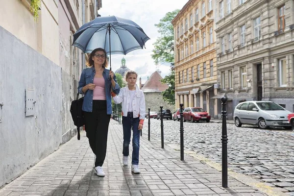 Мать и дочь идут под зонтиком вдоль улицы — стоковое фото