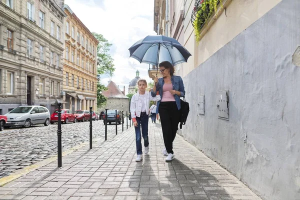 Matka a dcera kráčející pod deštníkem po ulici — Stock fotografie