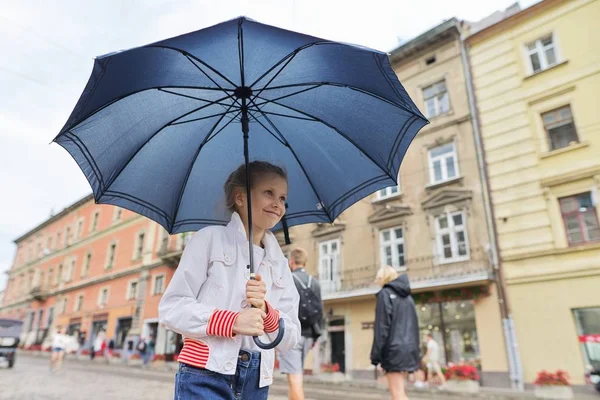 Kleines Mädchen, das mit einem Regenschirm auf einer Straße in der Stadt läuft — Stockfoto