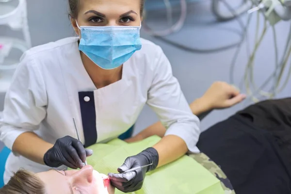 Female dentist treating teeth to patient, young man at dental clinic — Stock Photo, Image