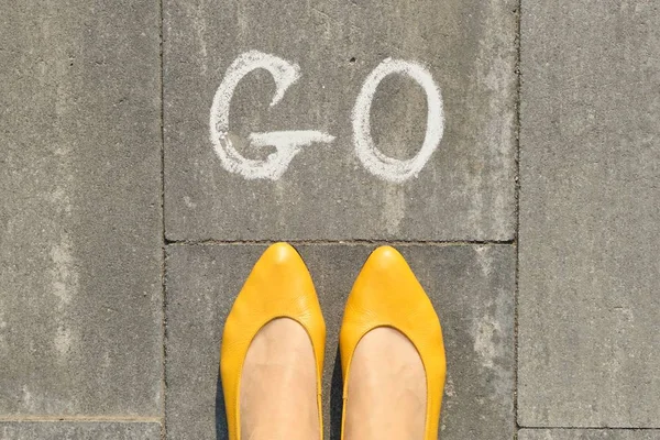 Slovo se píše na šedém chodníku s ženskýma nohama, pohled shora — Stock fotografie